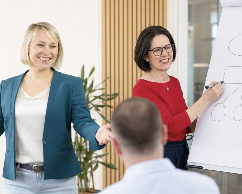 Anne Kühl spricht zur Gruppe, während Sandra Reithmayr live am Flipchart visualisiert